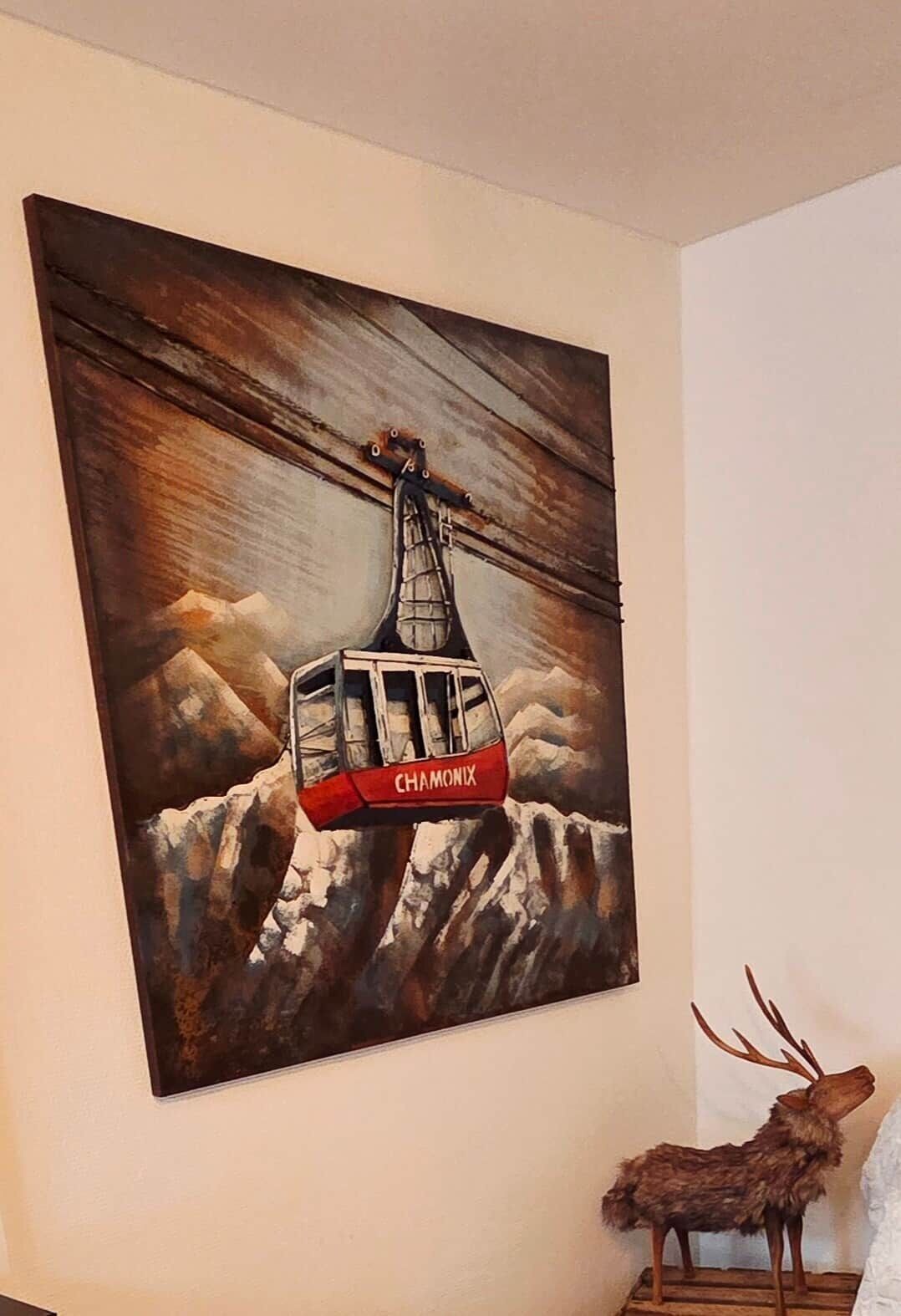 A painting of a cable car labeled "CHAMONIX" on a mountain backdrop.
