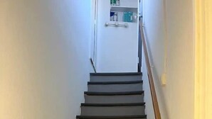 Een trap met een leuning, leidend naar een kamer met een witte deur en een plank met spullen.