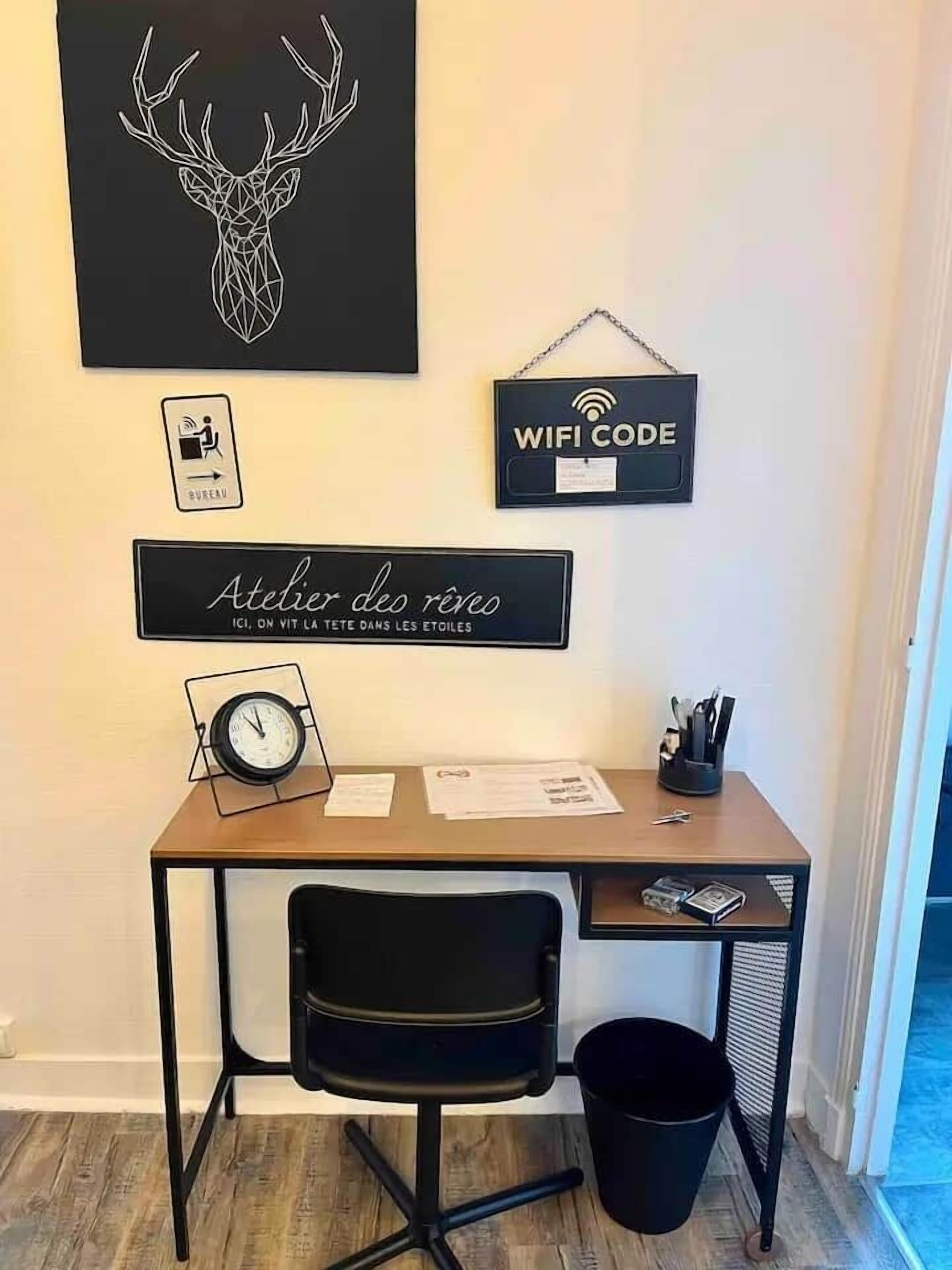 A small office space with a desk, chair, and a wall-mounted clock. There are signs for 'Atelier des Rêves' and 'WiFi Code'.