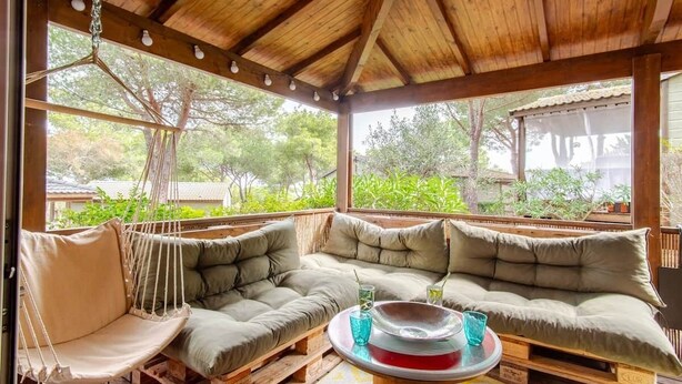 A covered outdoor seating area with a wooden ceiling, cushioned benches, and hanging chairs. - Mer et Pins - chalet with swimming pool (Agde)
