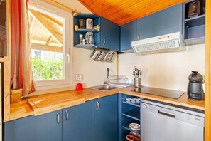 Une cuisine de taille réduite avec des meubles bleus, un lave-vaisselle et une fenêtre avec des rideaux.