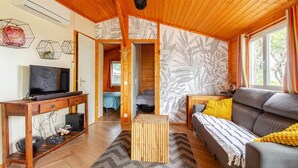 A cozy living room with a wooden ceiling, a sofa, a TV, and a patterned wall. - Mer et Pins - chalet with swimming pool (Agde)
