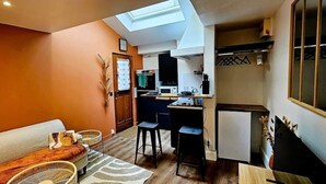 A compact living space with a sofa, a dining table, and a kitchenette. - La Cachette Oubliee (Melun)