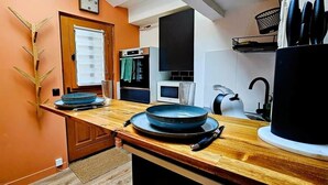 A compact kitchen with a wooden countertop, a microwave, a kettle, and a sink. - La Cachette Oubliee (Melun)