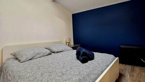 A bedroom with a bed, pillows, a nightstand, and a TV stand. - La Cachette Oubliee (Melun)