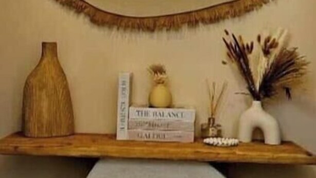 Un baño con inodoro, un espejo y un estante con un libro y objetos decorativos.