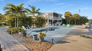 Una casa de dos pisos con piscina, rodeada de palmeras y un sendero pavimentado.
