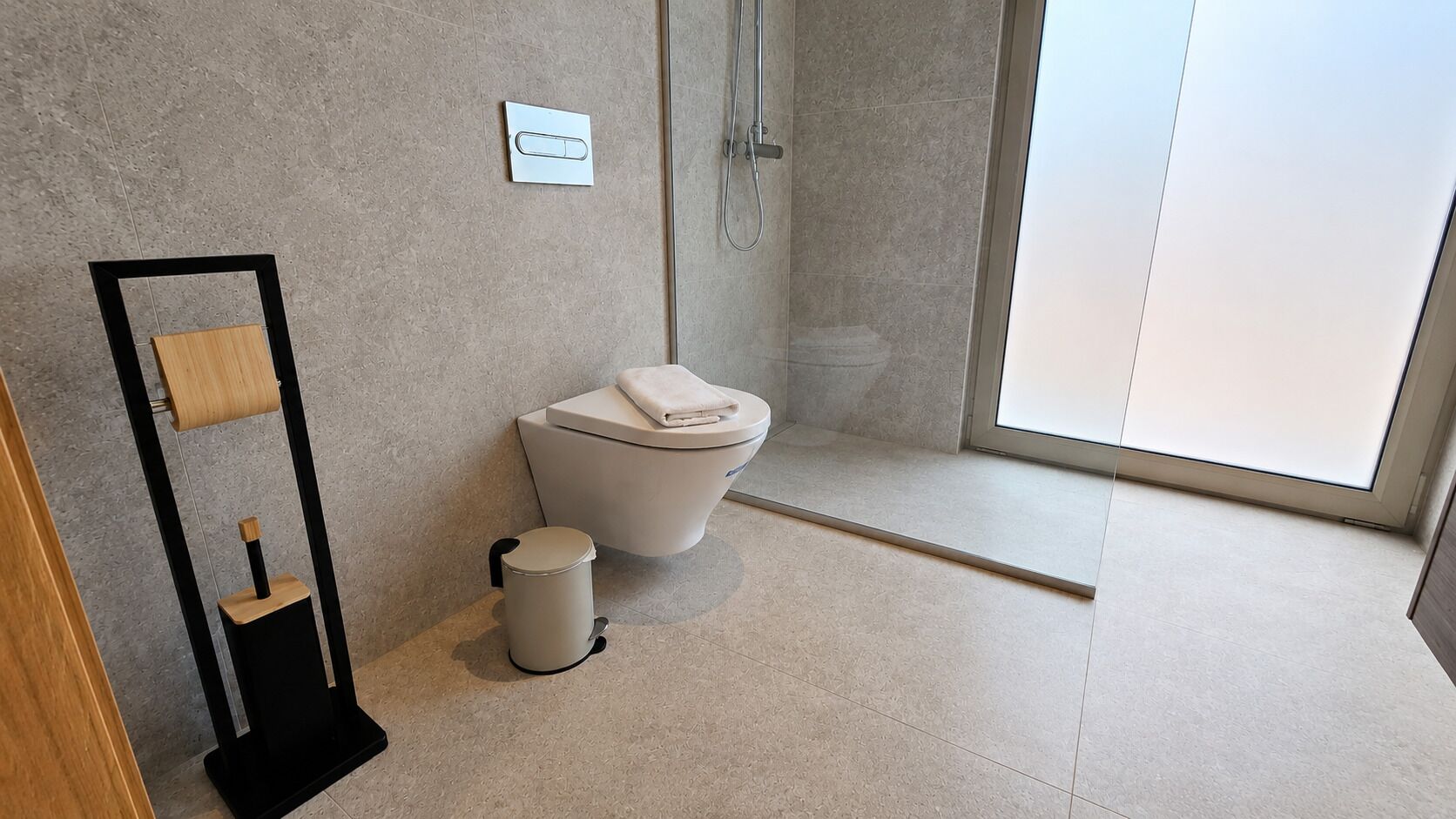 Un baño moderno con inodoro, un bote de basura, ducha y dispensador de toallas de papel.