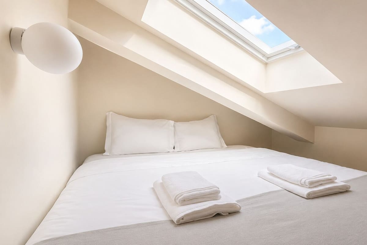 A bedroom with a skylight, a bed with white linens, and two folded towels on the bed.