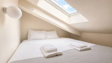 Een slaapkamer met een dakraam, een bed met witte lakens en twee opgevouwen handdoeken op het bed.