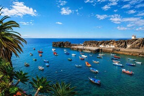 A coastal scene with boats docked at a pier, a lighthouse, and rocky cliffs. - Heritage Apartments (Câmara de Lobos)