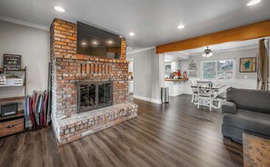 A living room with a brick fireplace, wooden flooring, a grey sofa, and a dining area with a table and chairs. - Donner Lake Delight – Truckee Retreat (Truckee)