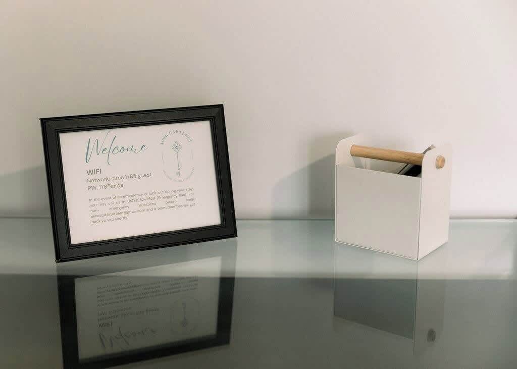 A framed welcome sign with WIFI and guest network information, a white storage box with a wooden handle, and a reflective surface.