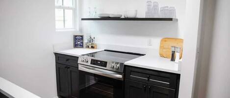 Una cocina moderna con armarios negros, estufa de acero inoxidable y encimera blanca.