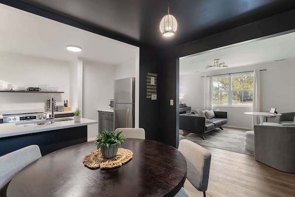 A modern kitchen with a central island, a dining area with a round table, and a living space with a sofa and a coffee table.