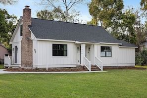 A single-story house with a brick chimney, white siding, and a dark roof.