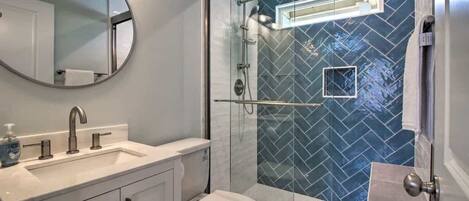 Une salle de bain moderne avec une douche à parois de verre, un lavabo blanc avec un miroir au-dessus et des toilettes.