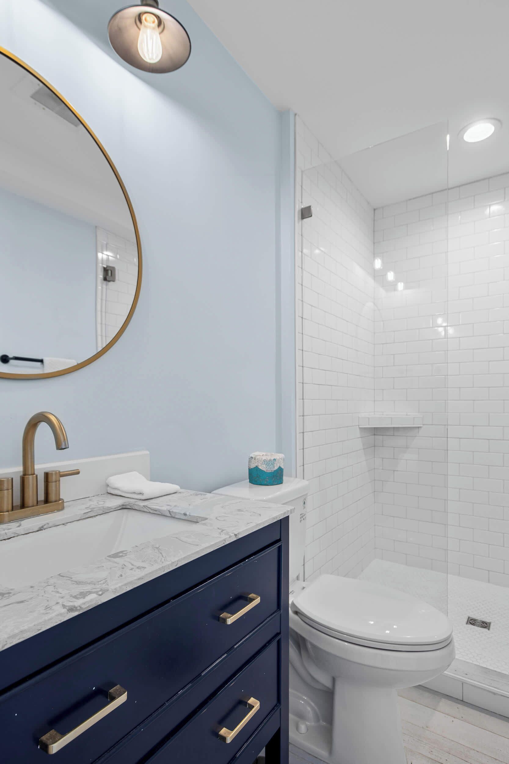 Une salle de bain avec un lavabo en marbre, un robinet doré, un meuble bleu foncé, des toilettes blanches et une douche à parois de verre.