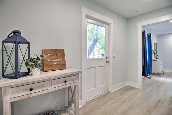 A hallway with a wooden sign reading "WELCOME TO BEAUTIFUL SCORT," a lantern, and a potted plant.