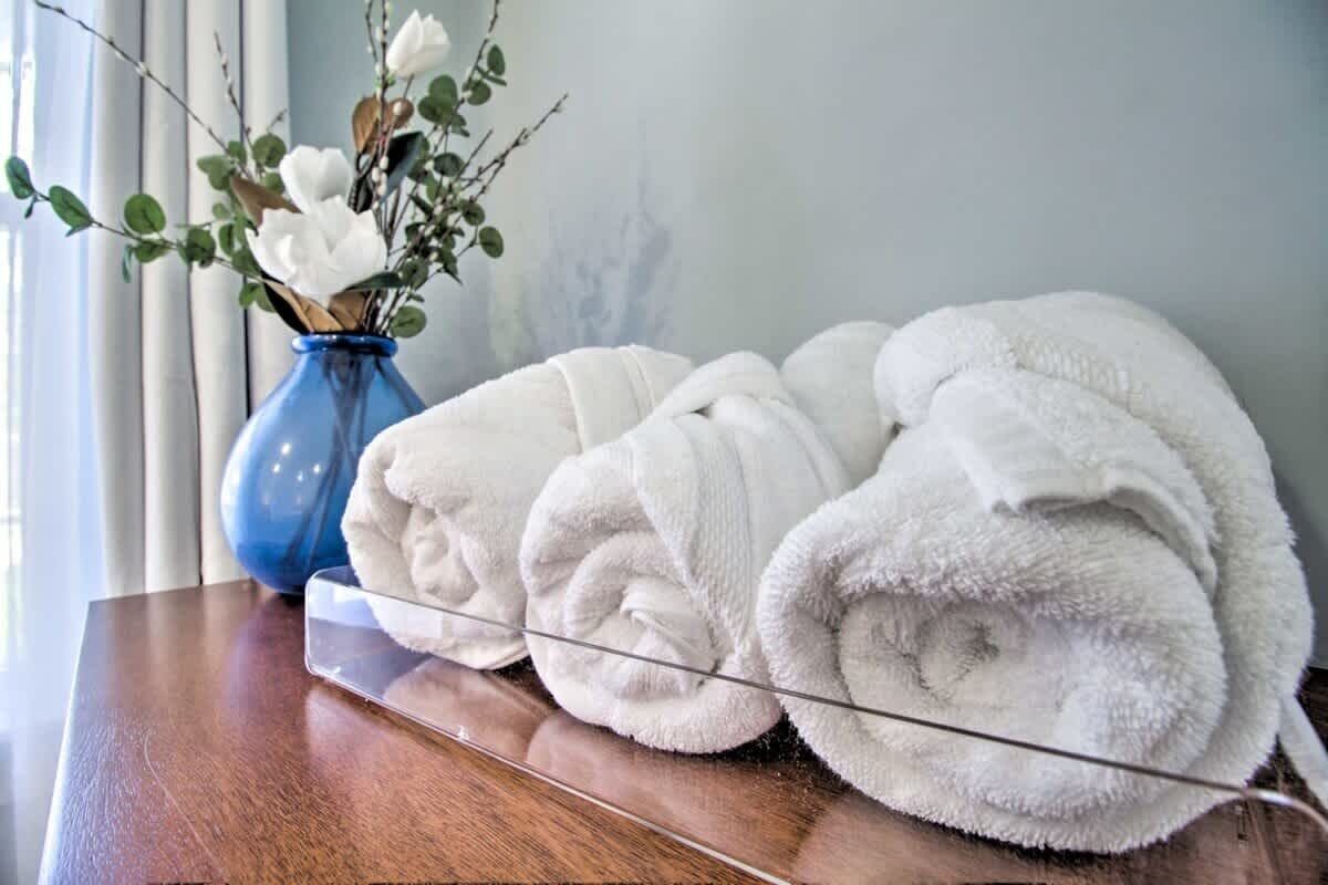 Superficie de madera con toallas blancas enrolladas y un florero azul con flores blancas.