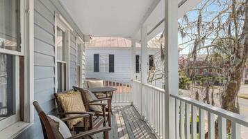 A porch with wooden chairs and a table, a white railing, and a view of a house and trees.