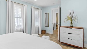 Ein Schlafzimmer mit Bett, Kommode, Spiegel und einem fenster mit Vorhängen.