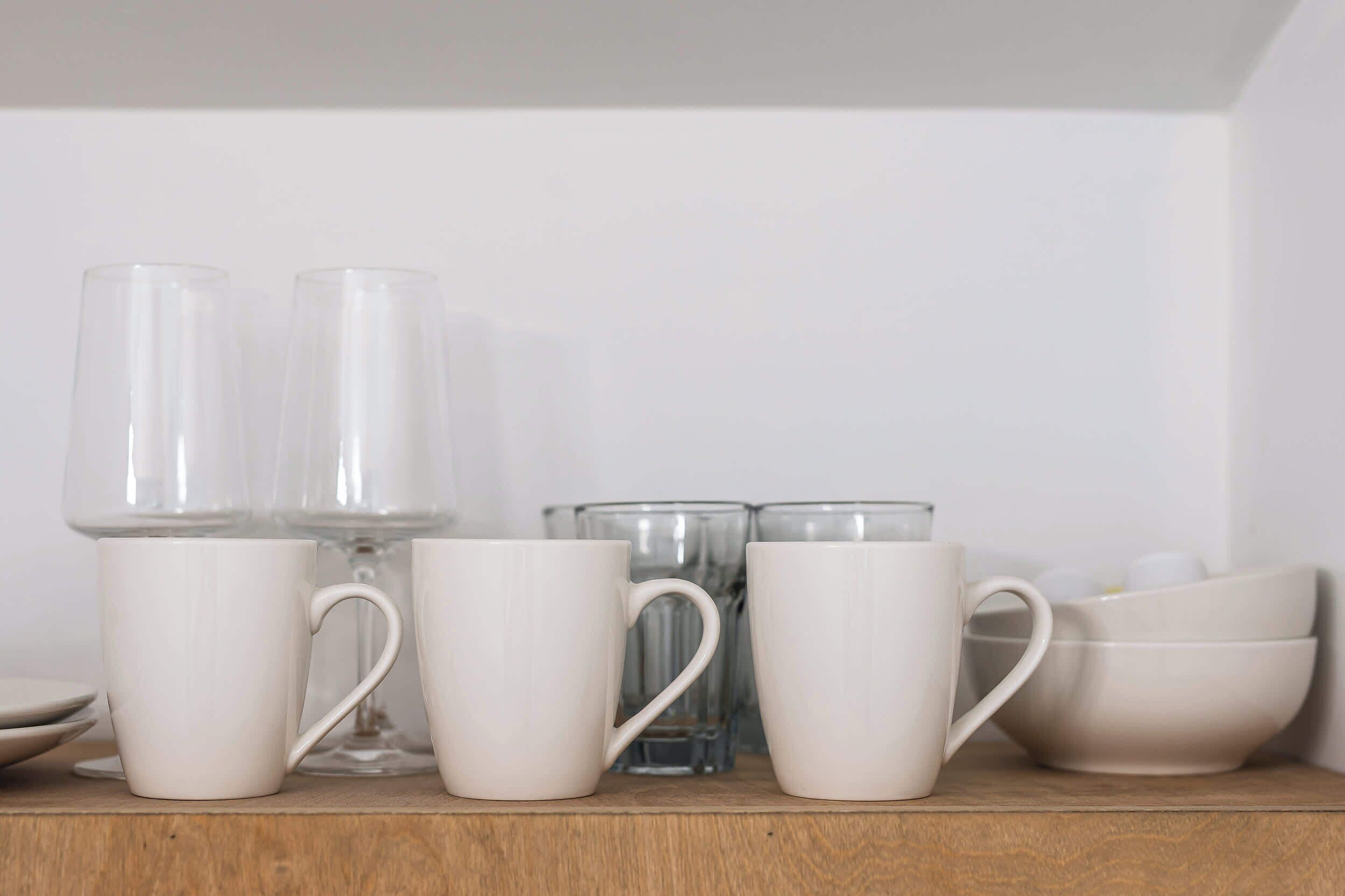A shelf with white ceramic mugs and clear glassware.