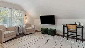 Ett modernt vardagsrum med en platt-TV, två fåtöljer, ett litet bord och ett stort fönster med persienner.