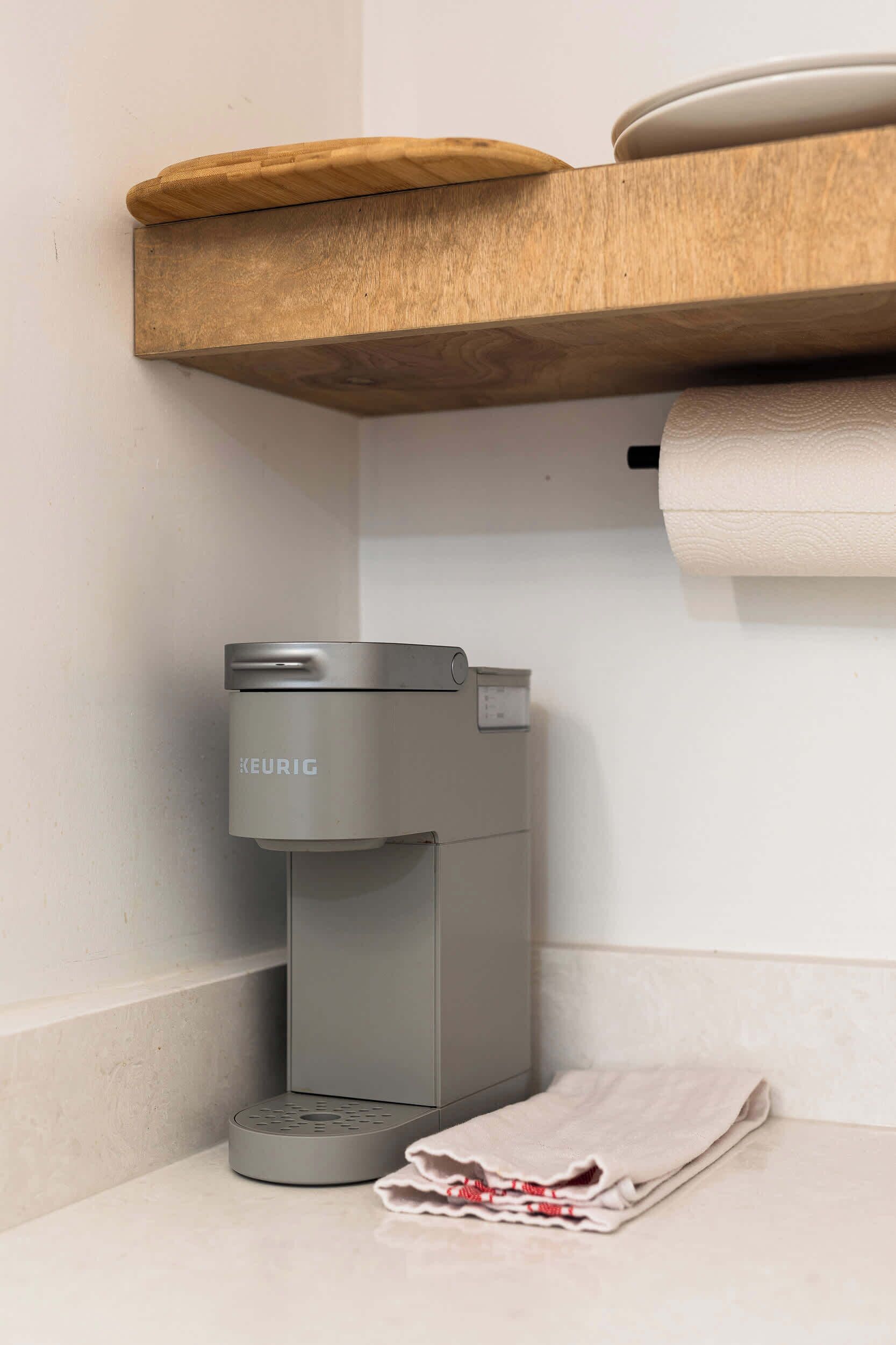A coffee maker, a towel, and a wooden shelf in a bathroom.