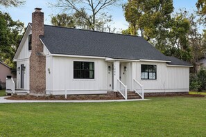 A single-story house with a brick chimney, white siding, and a front porch with steps.