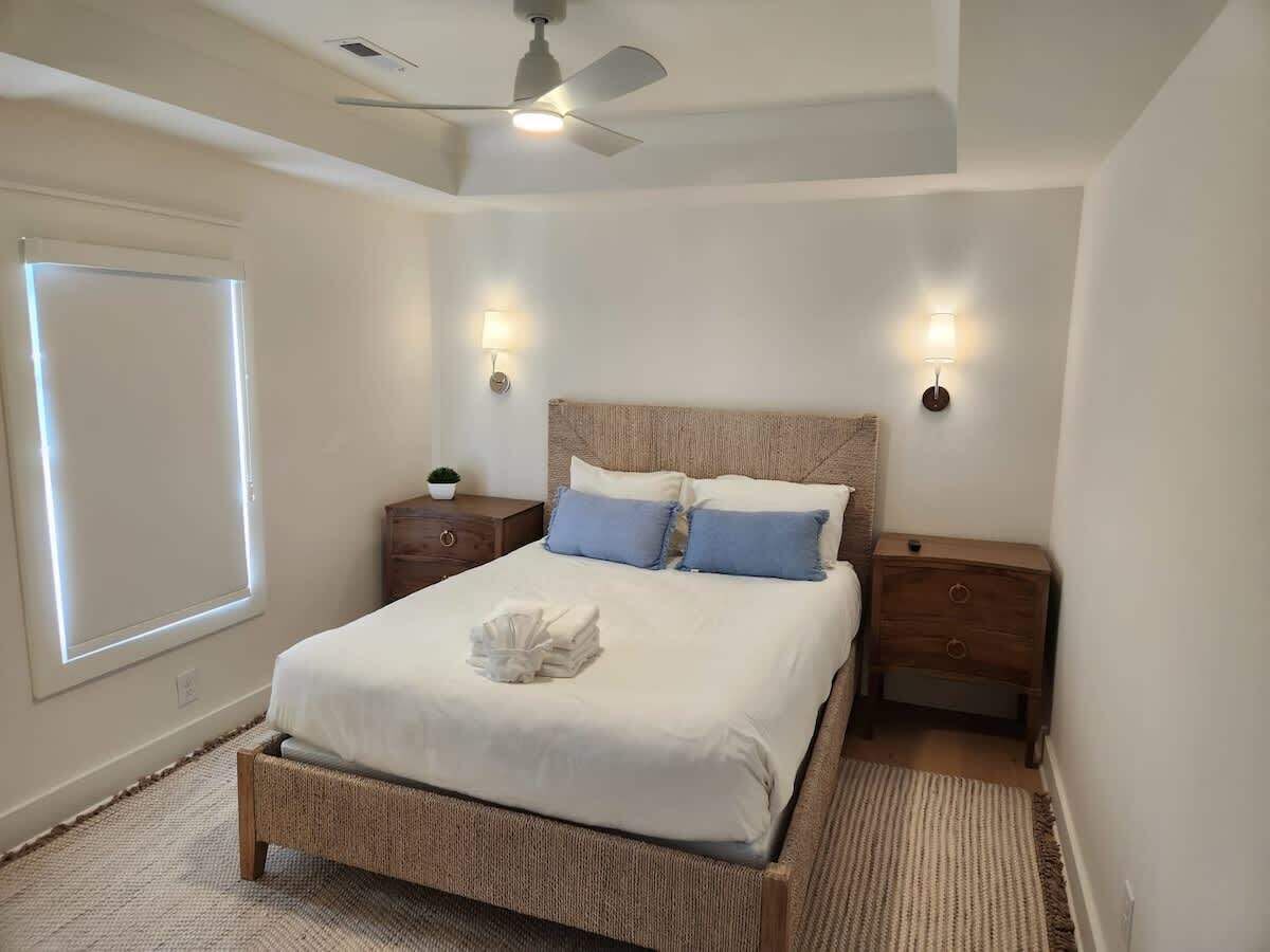 A neatly arranged bedroom with a bed, two bedside tables, a ceiling fan, and a window with blinds.