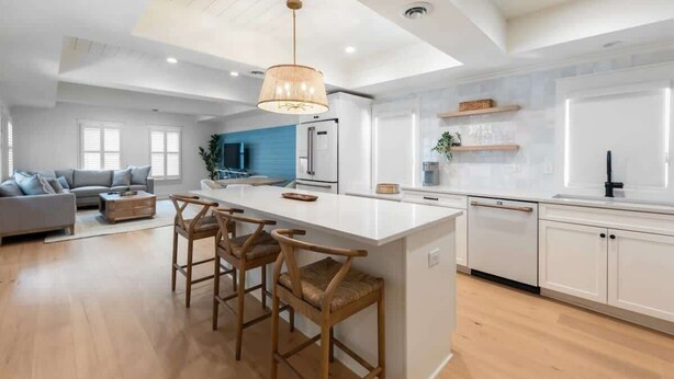 A spacious living area with a large island and bar stools, a kitchen with white cabinetry, and a blue accent wall. - Bright 2bd w. Chef's Kitchen, 1 Block to King! (Charleston)