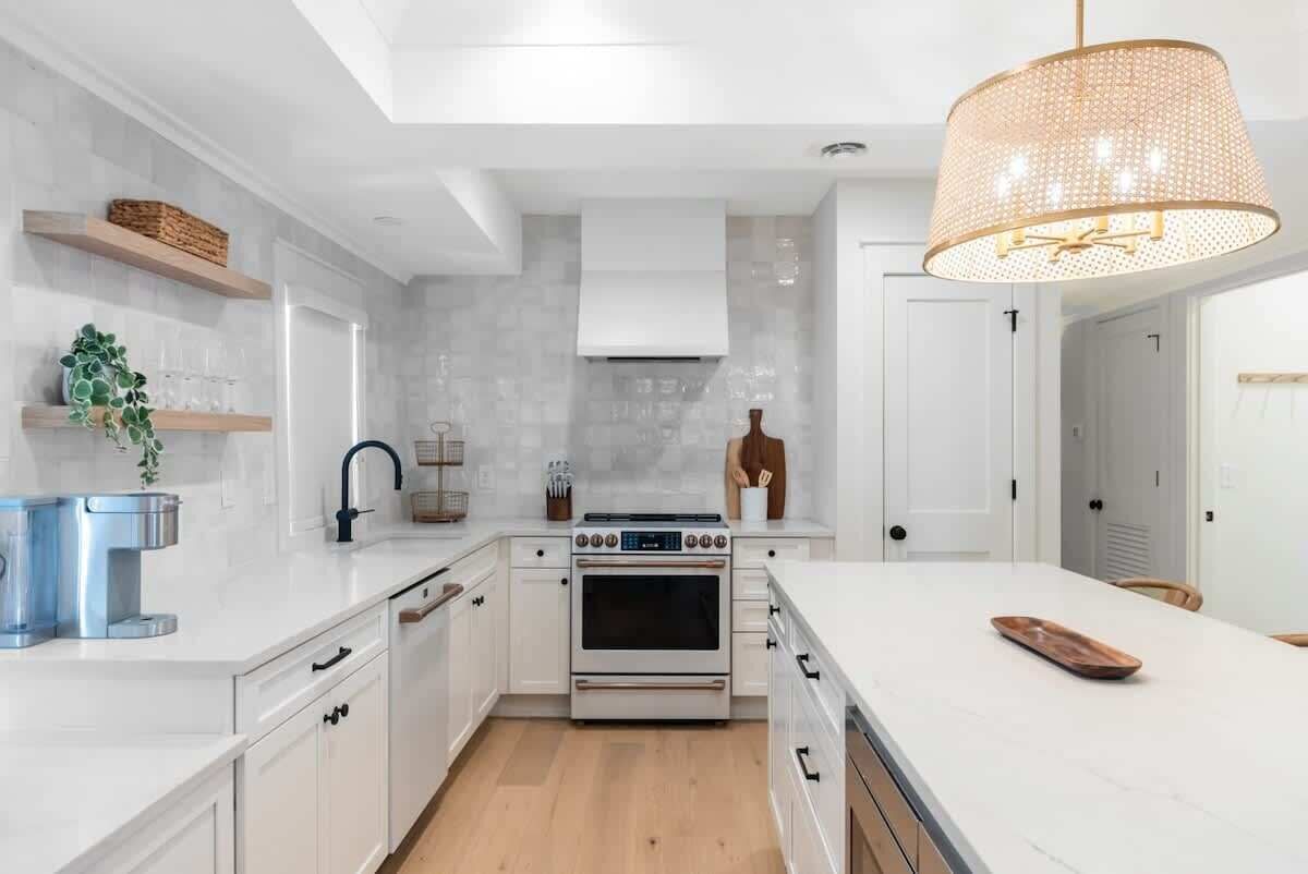 Une cuisine moderne avec des meubles blancs, un îlot central et un luminaire suspendu.