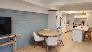 A modern kitchen with white cabinets, a wooden dining table with white chairs, and a built-in TV. - Bright 2bd w. Chef's Kitchen, 1 Block to King! (Charleston)