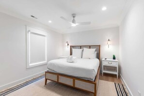 Une chambre à coucher comprenant un lit, des tables de chevet, un ventilateur de plafond et une fenêtre avec des stores.