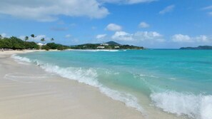A beach with clear turquoise water, a sandy shore, and a distant mountain. - OCEAN FRONT GENERATOR COMPELETION 11/1/2026 (East End)