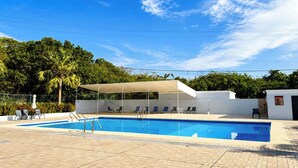 Ein Swimmingpool mit Liegestühlen und einem überdachten Bereich, umgeben von viel Grün.