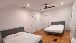 Un dormitorio con dos camas, suelo de madera, paredes blancas y un ventilador de techo.