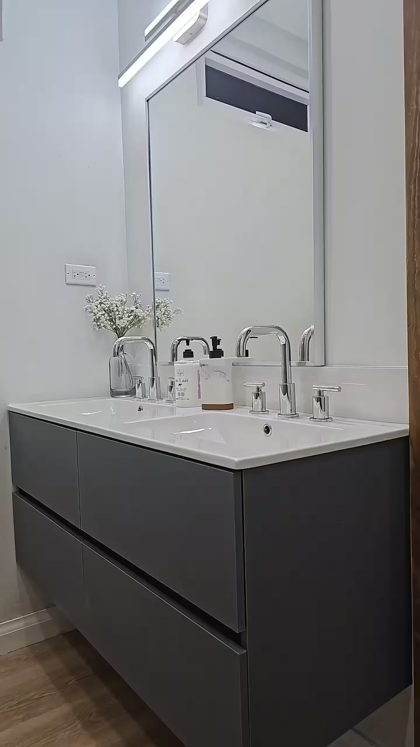 A modern bathroom with a double sink, a large mirror, and a dark-colored vanity.