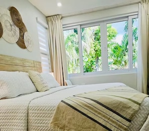 Ein Schlafzimmer mit einem großen Bett, einem Fenster mit Blick auf Grünflächen und einer Wand mit dekorativen Wandbildern.