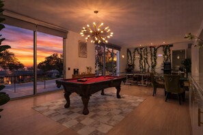 A modern living room with a pool table, large windows, and a decorative ceiling light.