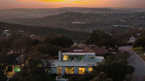 Ein modernes Haus mit einer großen Glasfassade, umgeben von Bäumen und einer hügeligen Landschaft im Hintergrund.