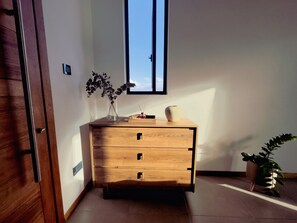 Un comò in legno con cassetti, un vaso con fiori secchi e una piccola pianta vicino a una finestra.