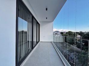 Un balcone con vista sulla città, ampie porte scorrevoli in vetro e un pavimento piastrellato.
