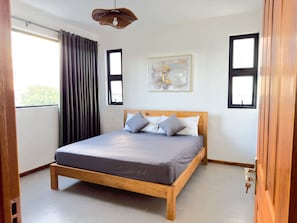 Una camera da letto con un letto in legno, biancheria grigia, una finestra con tende e una lampada a soffitto.