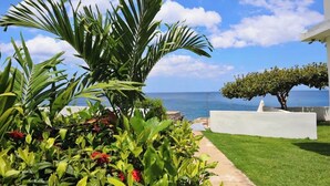 Ein Garten mit einer Palme, roten Blumen und Blick aufs Meer.