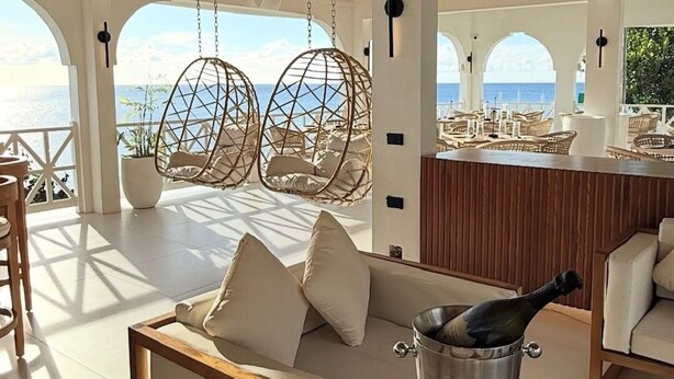 Eine Strandlounge mit einem Reetdach, Schaukelstühlen aus Korbmöbeln, einer Bar und Blick aufs Meer.