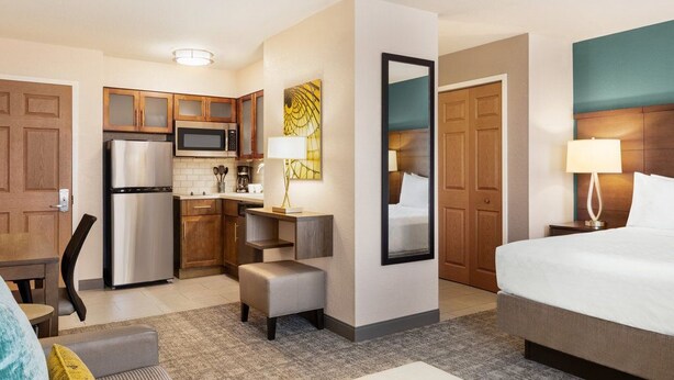 A hotel room with a bed, a desk, a kitchenette, and a bathroom.
