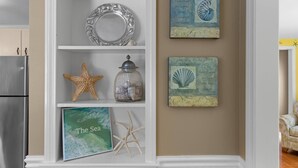Eine Küche mit weißen Schränken, einem Edelstahlkühlschrank und Dekorationselementen, darunter ein Seestern, ein Glas und ein gerahmtes Bild mit dem Titel "The Sea".