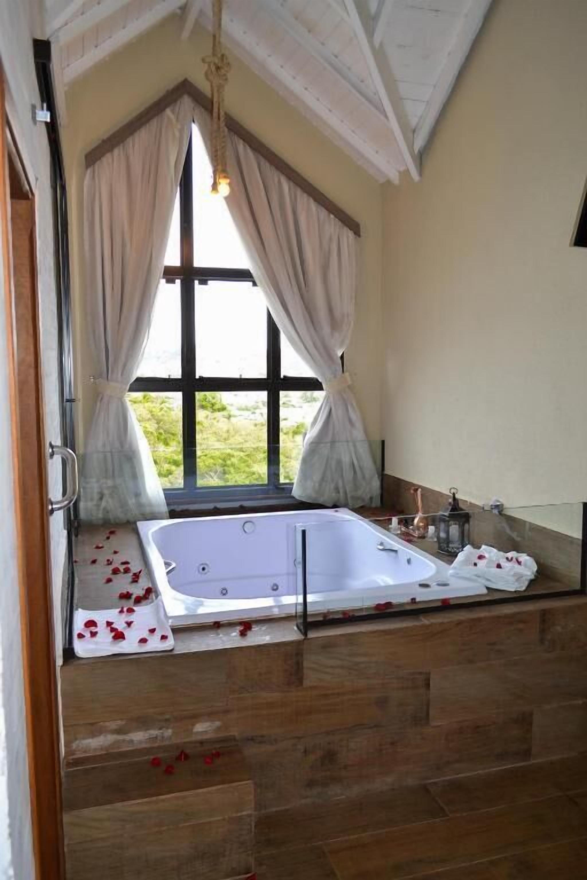 Casa de banho com banheira, janela com cortinas e vista para o exterior.